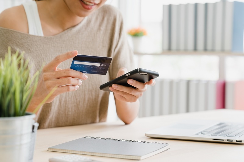 Woman holding phone on one hand and credit card on the other, depicting people shopping online.