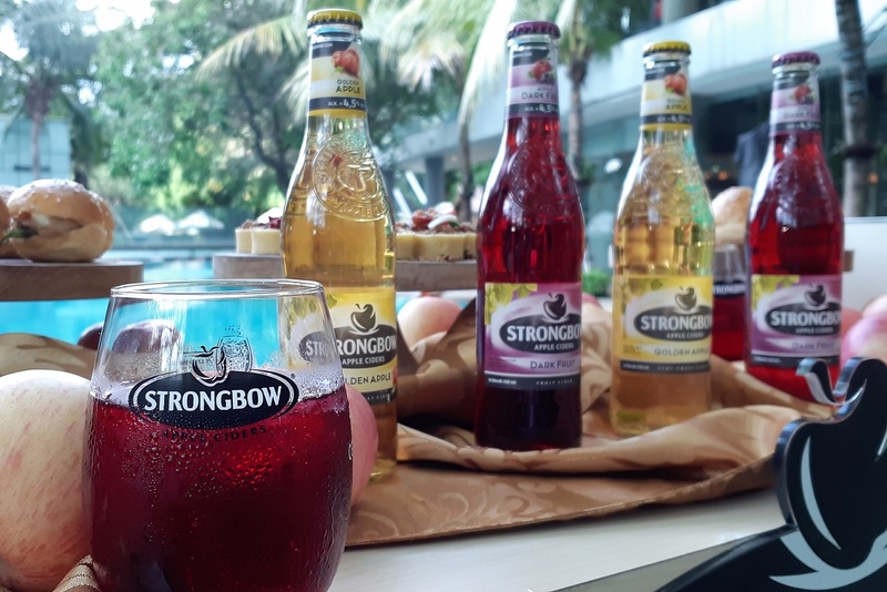 A glass of Strongbow's Dark Fruit on a table with fresh apples and four bottles of Strongbow new variants.