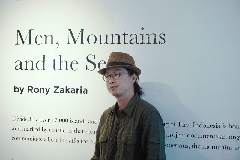 Rony Zakaria standing in front of a wall with his exhibition's title written on it.