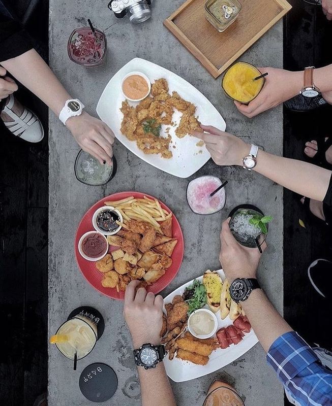 Various food on table with hands reaching for the foods at Bart Rooftop Bar at Artotel Thamrin.