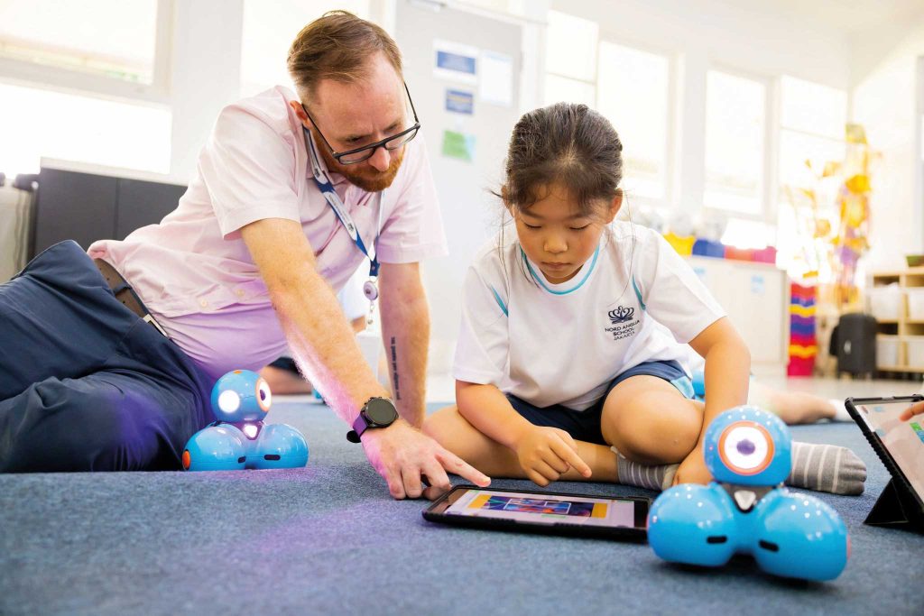 a nord anglia school jakarta teacher leans over and assists a younger student with an application on their tablet device