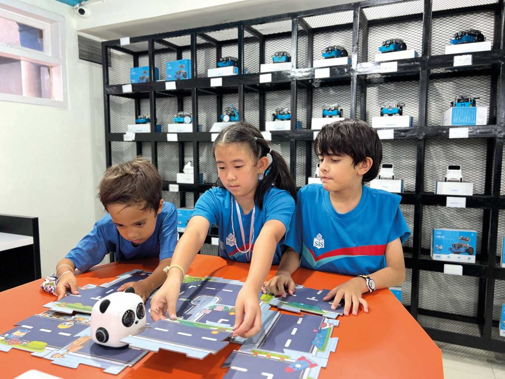 three SIS South Jakarta students place roads down in a robotics class.